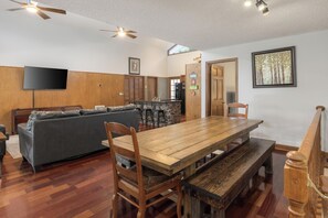 A spacious living area with a wooden dining table, a grey sofa, and a television mounted on the wall. - Perfect Getaway on the Water~Beautiful Gorge Views~11 miles to Downtown! (Chattanooga)