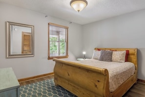 A bedroom with a wooden bed, a nightstand with a lamp, a window with blinds, and a mirror on the wall. - Perfect Getaway on the Water~Beautiful Gorge Views~11 miles to Downtown! (Chattanooga)