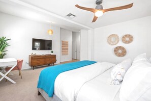 Quarto com cama, escrivaninha, penteadeira, ventoinha no teto e decorações nas paredes.