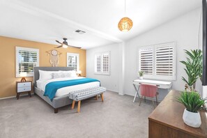 Ein Schlafzimmer mit Bett, Nachttisch, Schreibtisch, Stuhl und Deckenventilator.