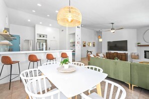 Eine moderne Küche mit weißen Schränken, ein Essbereich mit weißen Stühlen und ein grünes Sofa.