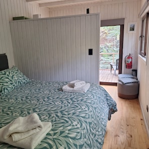 A bedroom with a large bed, a door leading to a balcony, and a fire extinguisher mounted on the wall. - Casa Verde Hostal Ecologico (Curacautin)