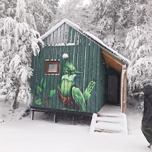 Una cabaña de madera cubierta de nieve con un mural de un colibrí en la fachada.
