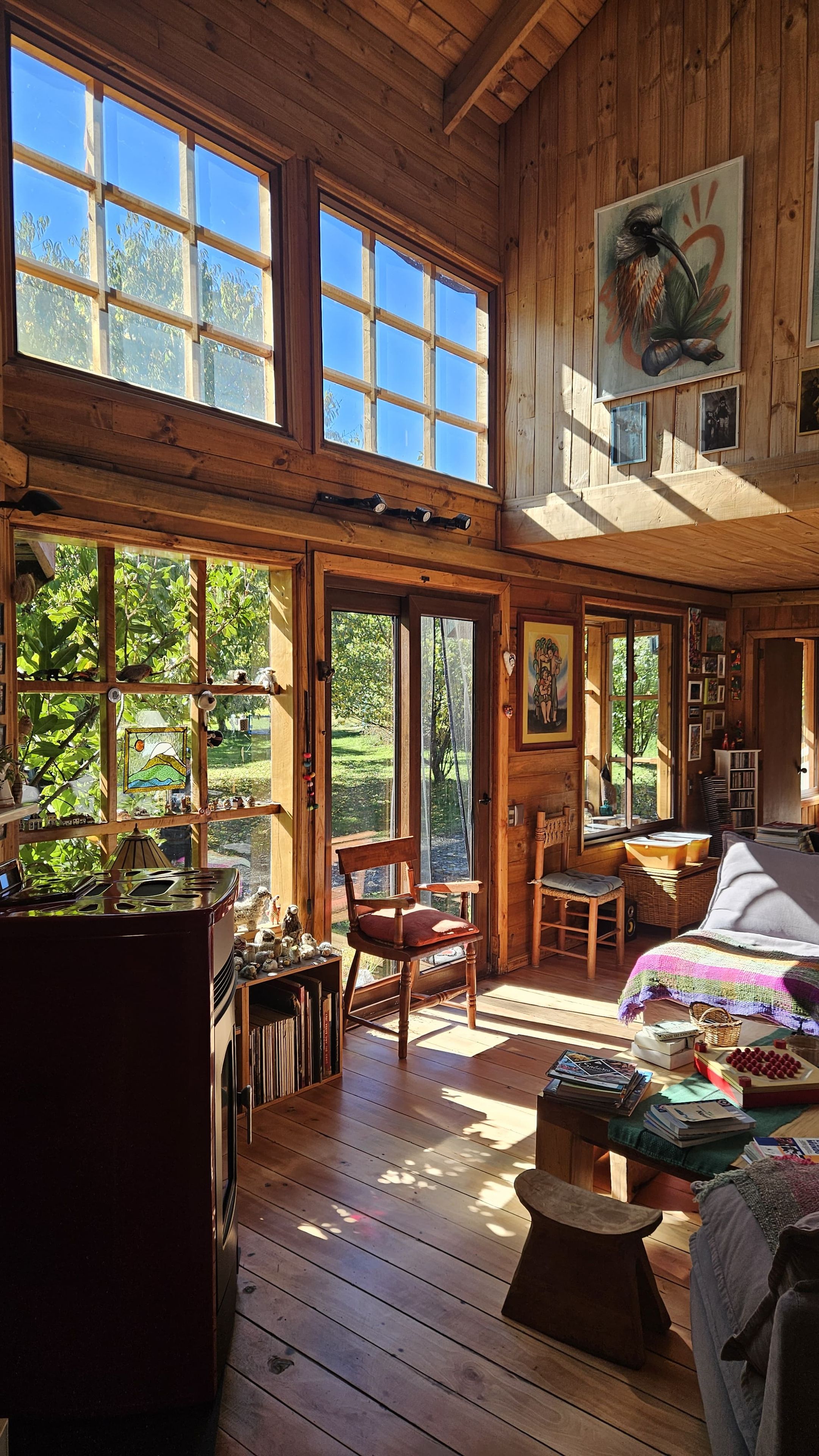 Interior de una cabaña de madera con ventanas grandes, un comedor y una zona de estar acogedora.
