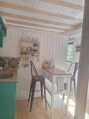 A kitchen with a wooden ceiling, a shelf with kitchenware, a dining table with chairs, and a window. - Casa Verde Hostal Ecologico (Curacautin)