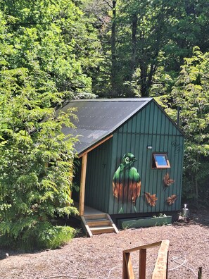 A green shed with a small window and a wooden staircase leading up to it, surrounded by dense foliage. - Casa Verde Hostal Ecologico (Curacautin)