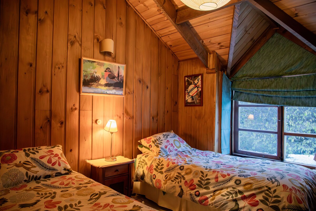 A wooden room with two beds, a nightstand, a lamp, and a framed poster on the wall.