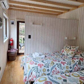 A bedroom with a bed, a fire extinguisher, and a door leading to an outdoor area. - Casa Verde Hostal Ecologico (Curacautin)