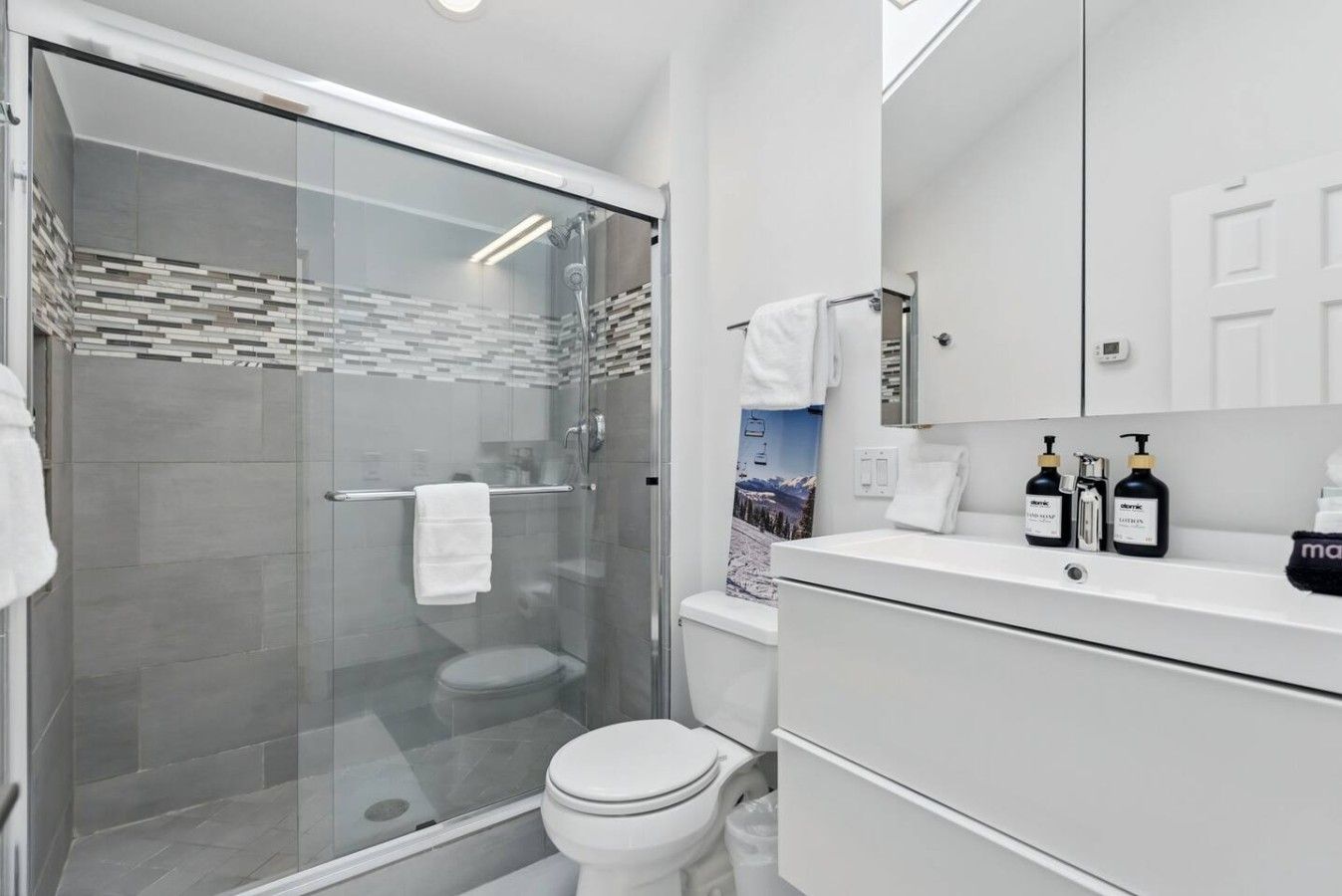 Ein modernes Badezimmer mit einer Duschkabine aus Glas, einer Toilette und einem Waschtisch mit Spiegel und Pflegeprodukten.