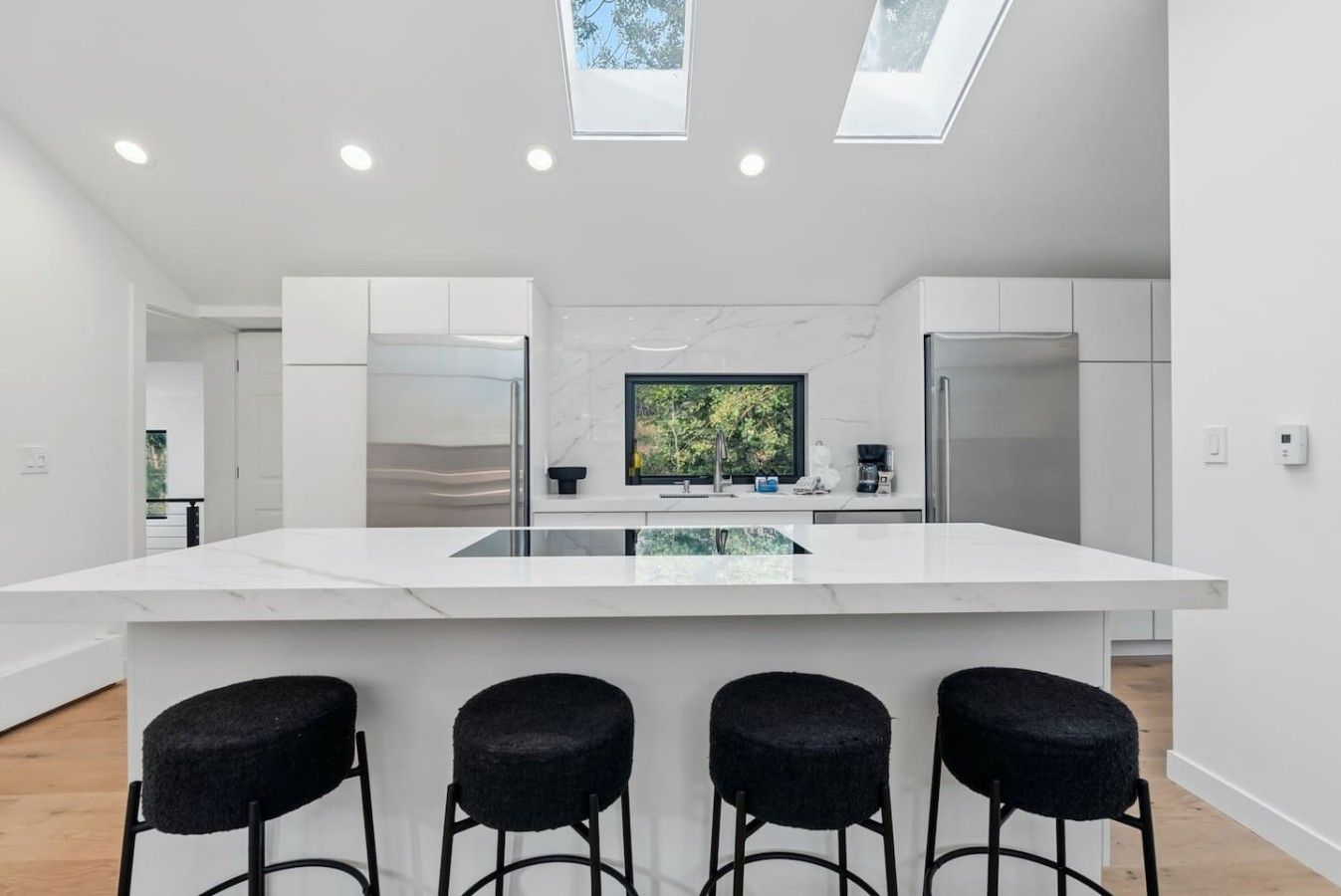 Een moderne keuken met een centraal eiland, barkrukken, dakramen en uitzicht op groen.