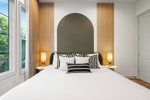A modern bedroom with a large bed, two bedside lamps, and a view of greenery outside. - Pickleball, Game Room, Firepit, Putt putt, Hot Tub (Leicester)