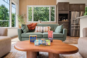 A modern living room with a green sofa, a wooden coffee table, and board games. - Pickleball, Game Room, Firepit, Putt putt, Hot Tub (Leicester)
