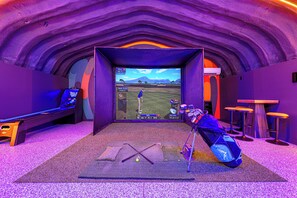 Een kamer met een golfsimulatie, inclusief een scherm waarop een golfspel te zien is, een golfkar en een golftas.