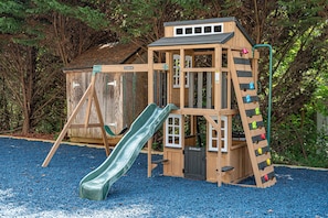 Een houten speelconstructie met een glijbaan en een klimgedeelte, omringd door bomen.