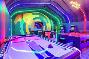 Een pooltafel in een neonverlichte omgeving, een dartbord en speelautomaten.