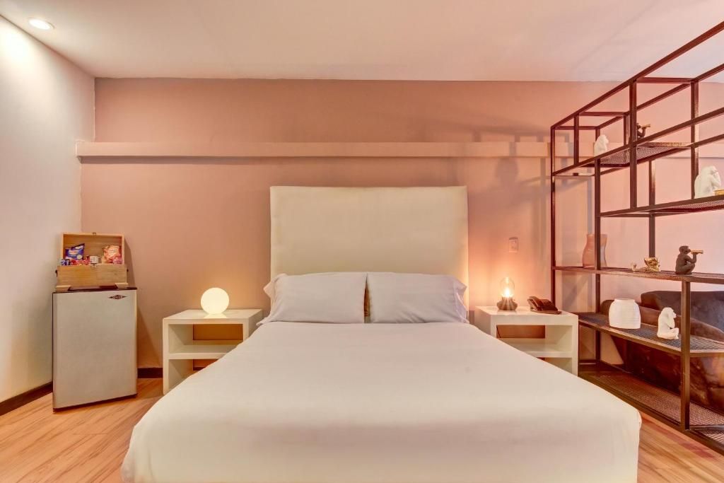 Une chambre d’hôtel comprenant un lit, des tables de chevet, un petit réfrigérateur et une étagère.
