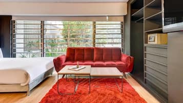 Ein modernes Zimmer mit einem roten Sofa, einem Holztisch und einem großen Fenster mit Jalousien.