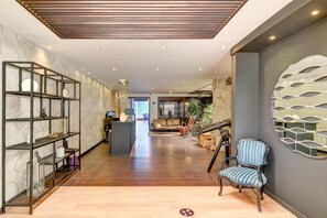 Un pasillo espacioso con techo de madera, una zona de estar con un sofá y una silla, y una pared decorativa con un diseño geométrico.