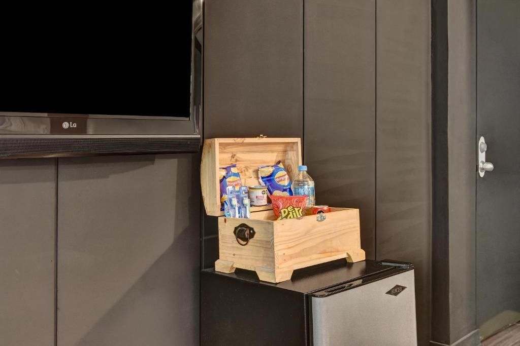 Eine kleine Holzkiste mit Snacks und Getränken steht auf einem schwarzen Gerät, wahrscheinlich einem Minikühlschrank, in einem Raum mit dunkelholzbepflanzten Wänden und einem flachbildfernseher, der darüber angebracht ist.