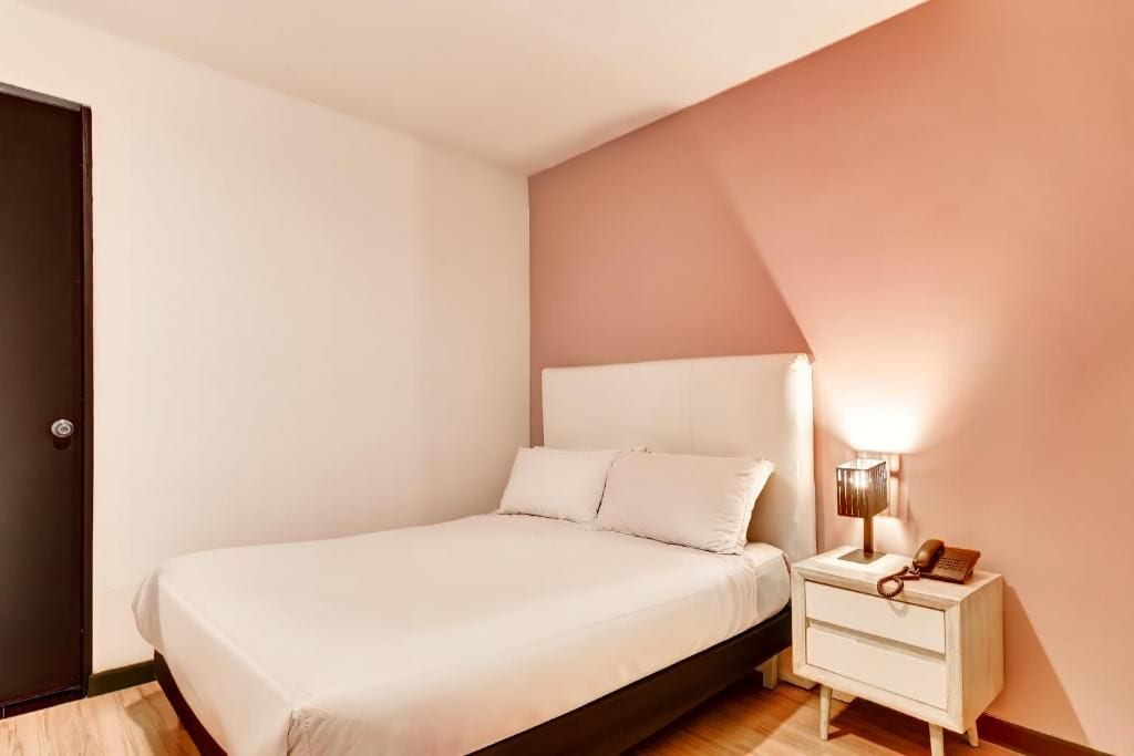Un dormitorio con cama, mesita de noche, lámpara y una puerta.