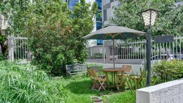 Un espacio al aire libre con una mesa y sillas, rodeado de vegetación y una cerca blanca.