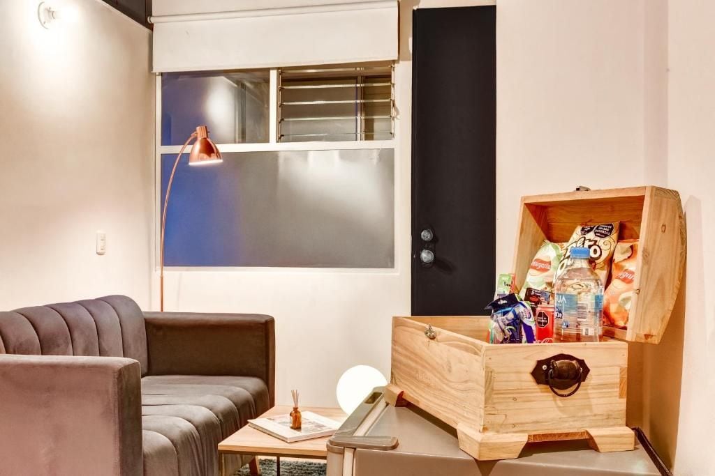 Un espacio habitable compacto con sofá, una mesita, un cofre de madera y una ventana con persianas.