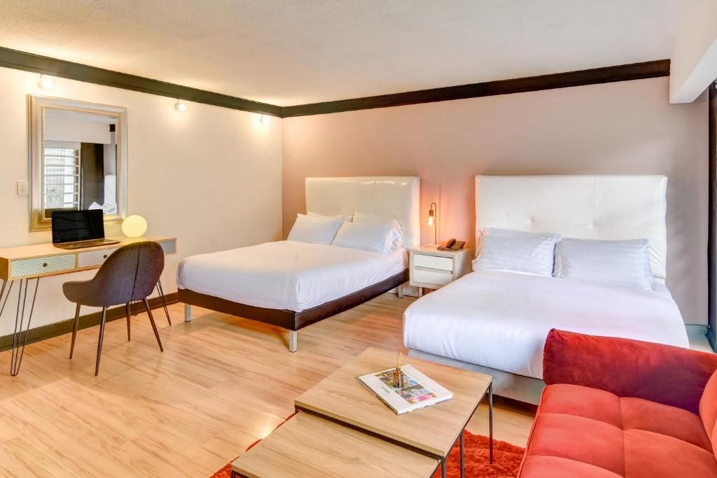 A hotel room with two beds, a desk, a chair, a red sofa, and a mirror.