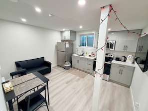 A compact kitchen with modern appliances, a dining area with a table and chairs, and a sofa. - Brand-New Legal Suite | East Regina (Regina)