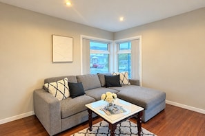A living room with a grey sectional sofa, a coffee table with magazines, and a framed picture on the wall. - Million Dollar View (Wellington)