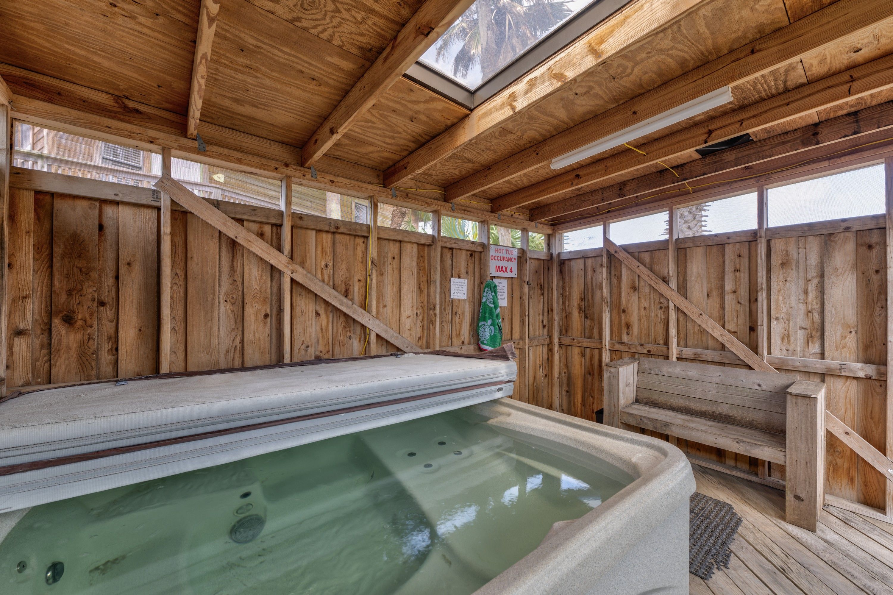 A wooden spa area with a hot tub, wooden walls, and a skylight.