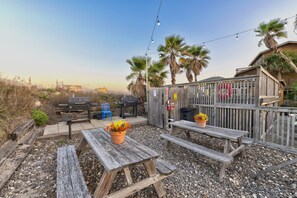 Une terrasse avec des bancs en bois, un barbecue et une guirlande lumineuse.