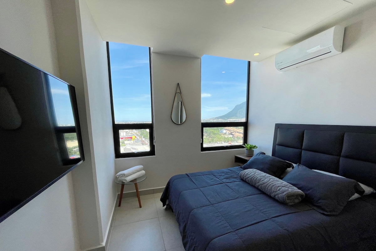 Un dormitorio con cama, dos ventanas, una planta en maceta y aire acondicionado de pared.