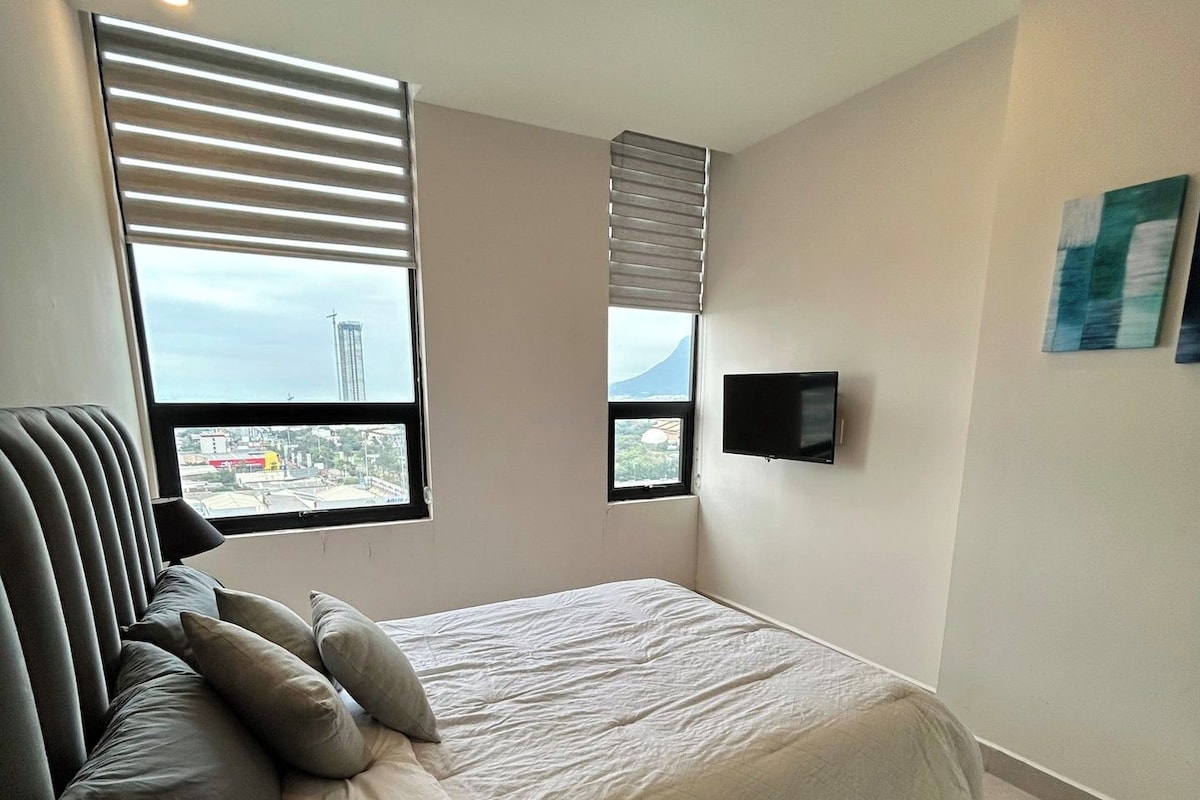 Un dormitorio moderno con una cama, un sillón, un televisor y vistas a la ciudad.