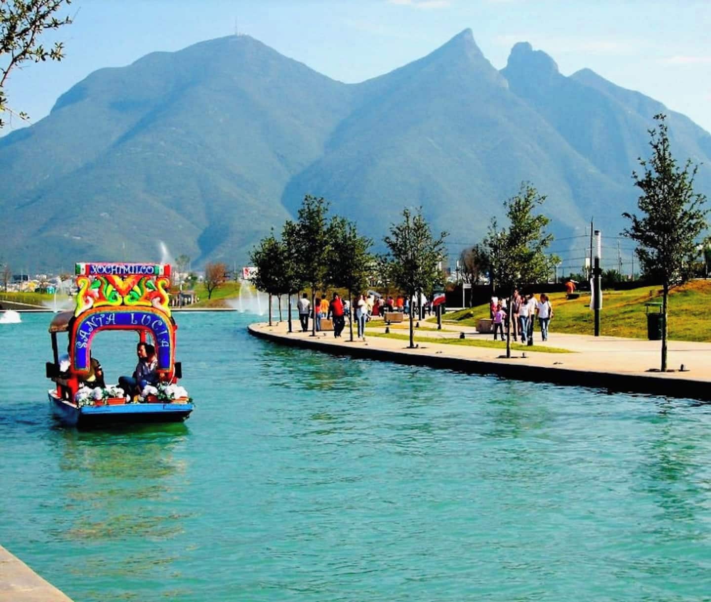 A boat with a colorful archway labeled 'Santa Lucia' on a body of water with mountains in the background.
