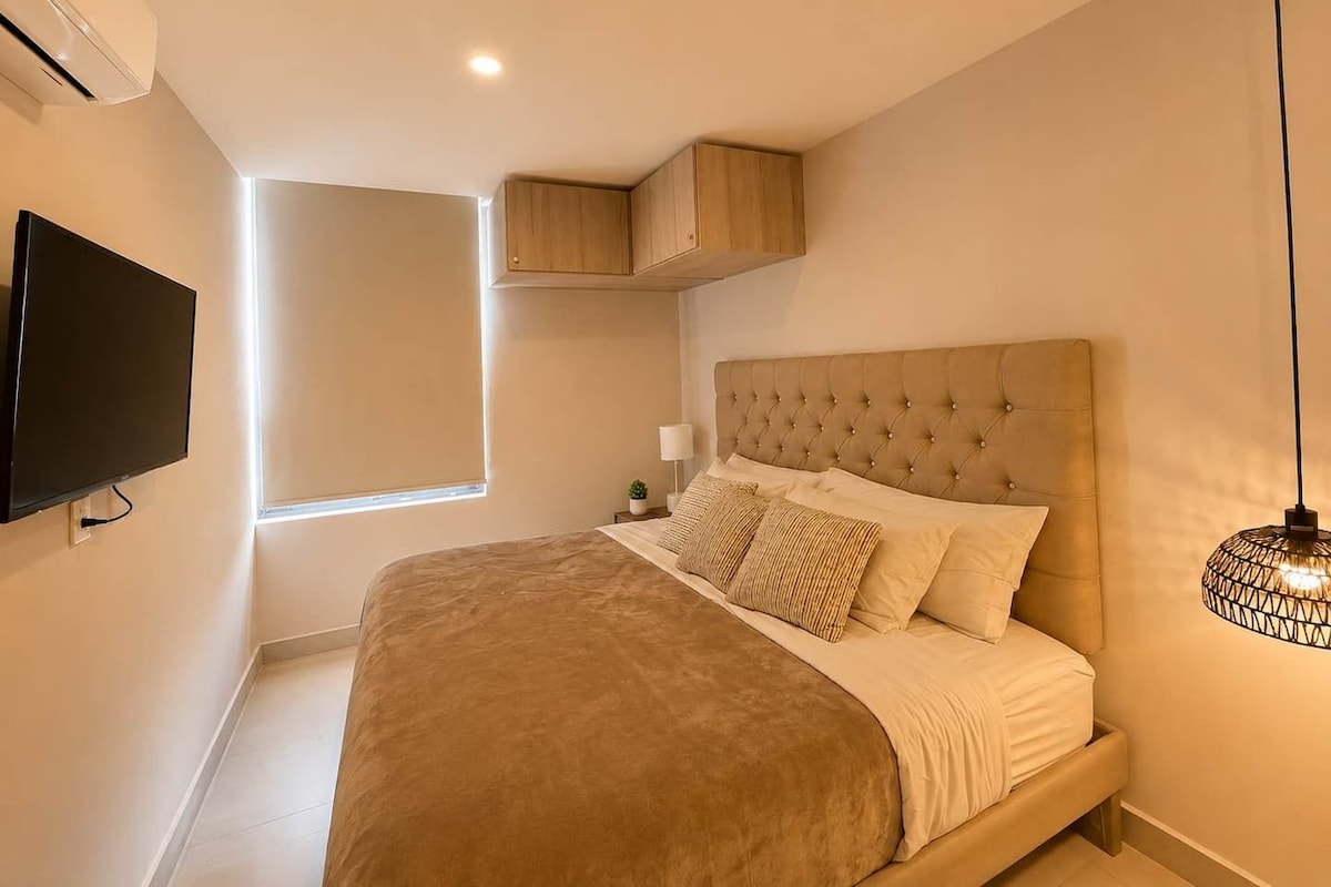 A bedroom with a large bed, a television mounted on the wall, and a window providing natural light.
