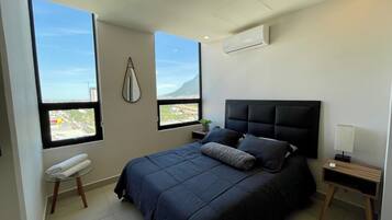 Un dormitorio moderno con una cama grande, dos ventanas, una mesita de noche y un equipo de aire acondicionado.