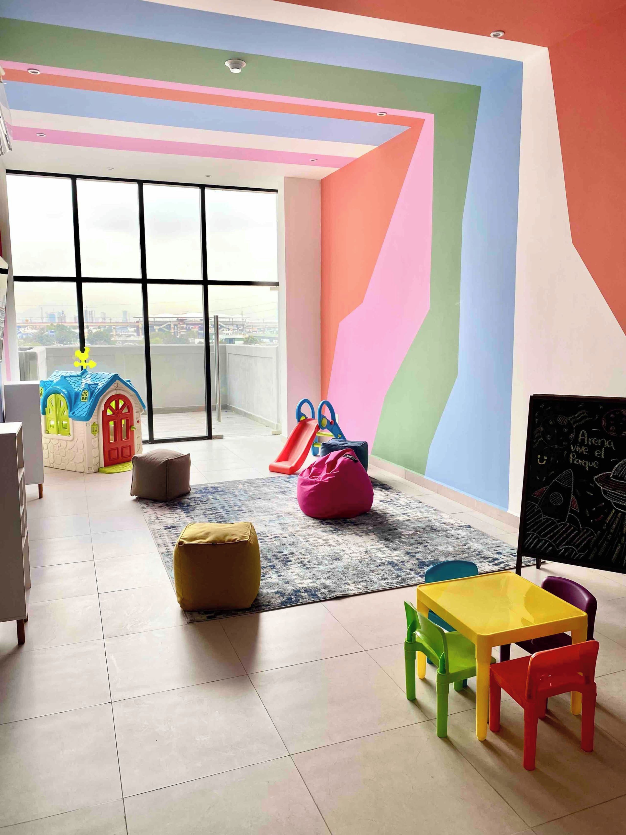 Una habitación de colores vivos con una zona de juegos, un ventanal grande y una pizarra.