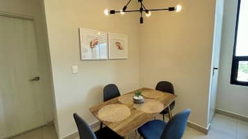 A dining area with a wooden table, blue chairs, a modern pendant light, and two framed artworks on the wall.