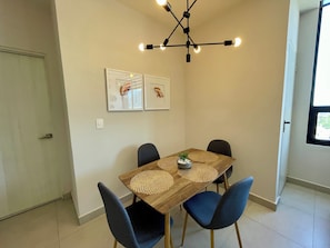 Un comedor con una mesa de madera, sillas azules, una lámpara colgante moderna y dos cuadros en la pared.
