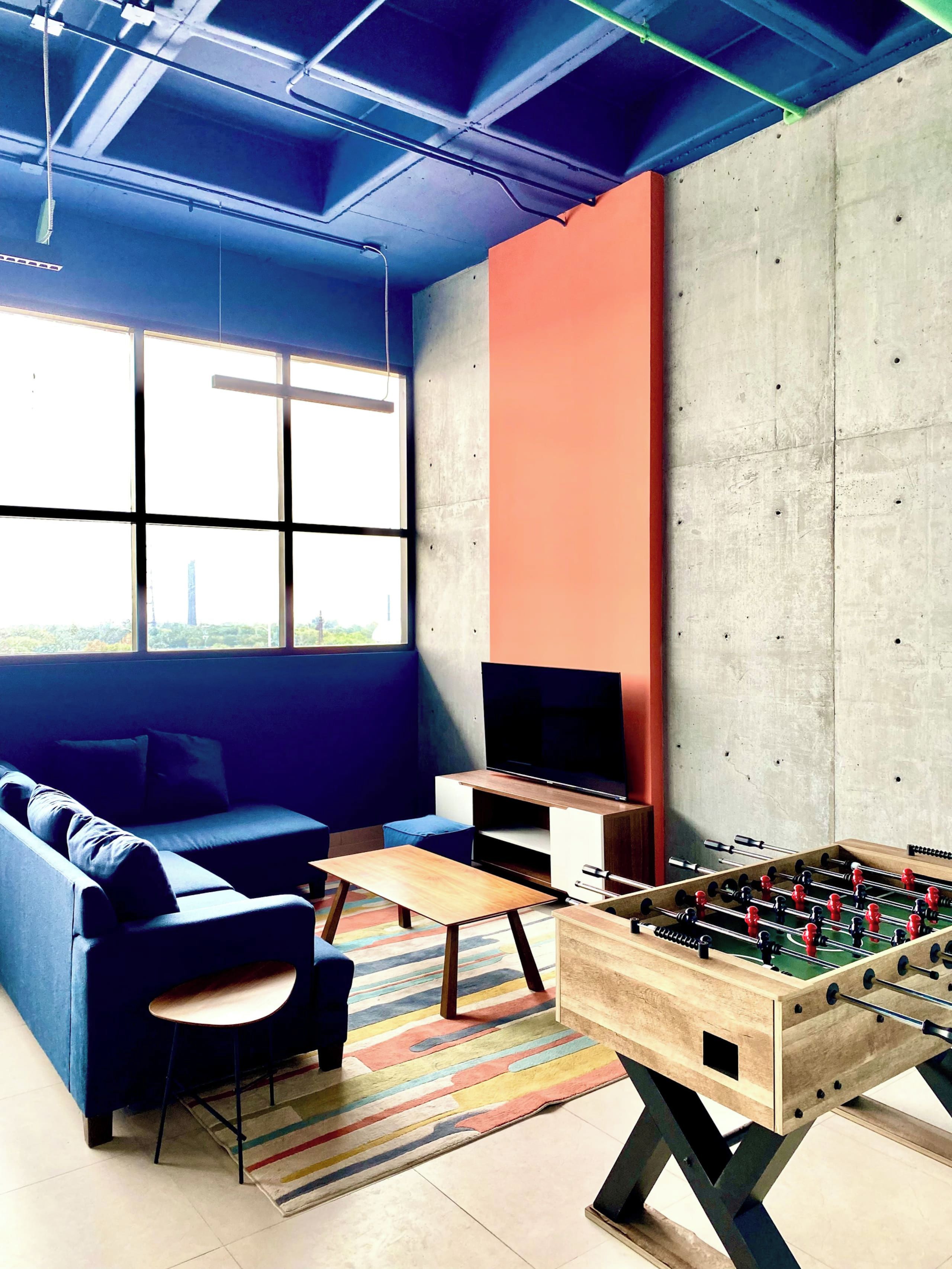 A room with a sofa, television, foosball table, and a large window.