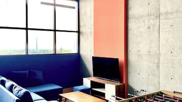 A room with a sofa, television, foosball table, and a large window.
