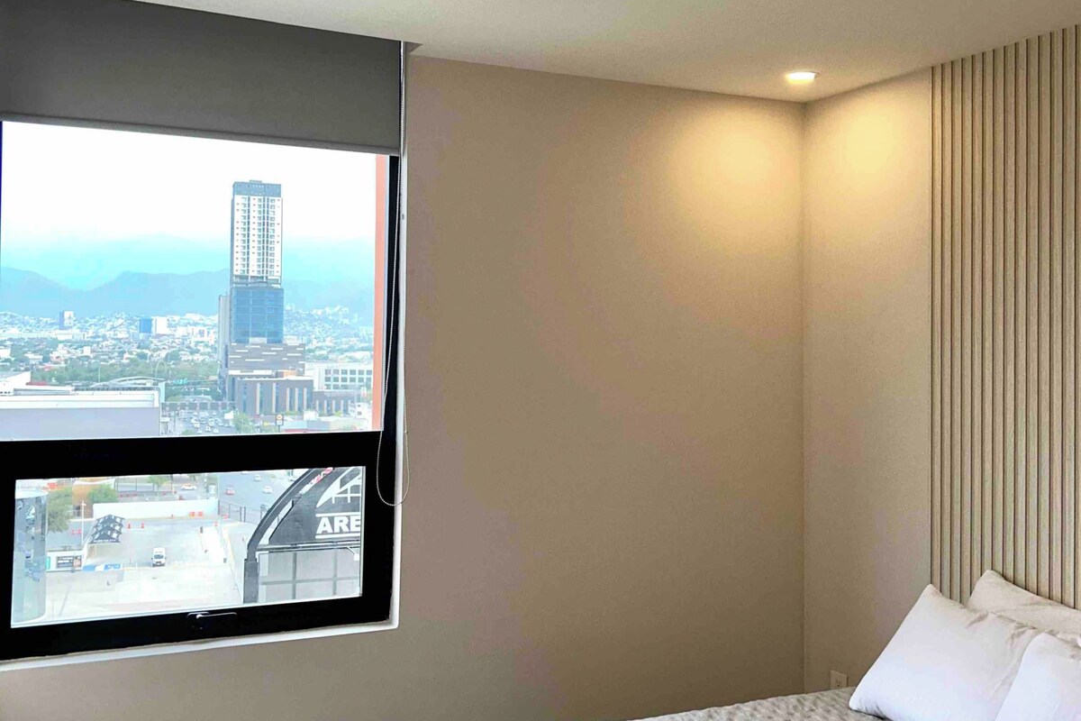 Una habitación de hotel con cama, ventana con vista a la ciudad e iluminación empotrada en el techo.