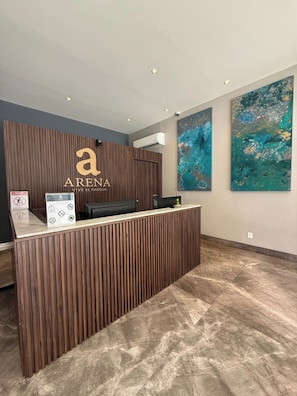 Un mostrador de recepción con detalles de madera, un logotipo y un cartel con iconos. Hay dos cuadros abstractos en la pared.
