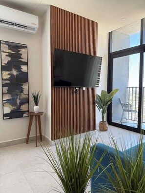Una sala moderna con un televisor de pantalla plana montado en una pared de paneles de madera, un cuadro abstracto grande y una planta en maceta.