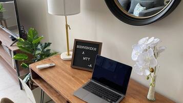 A wooden desk with a laptop, a 'BIENVENIDOS A MTY' sign, a lamp, a vase with white flowers, and a mirror.