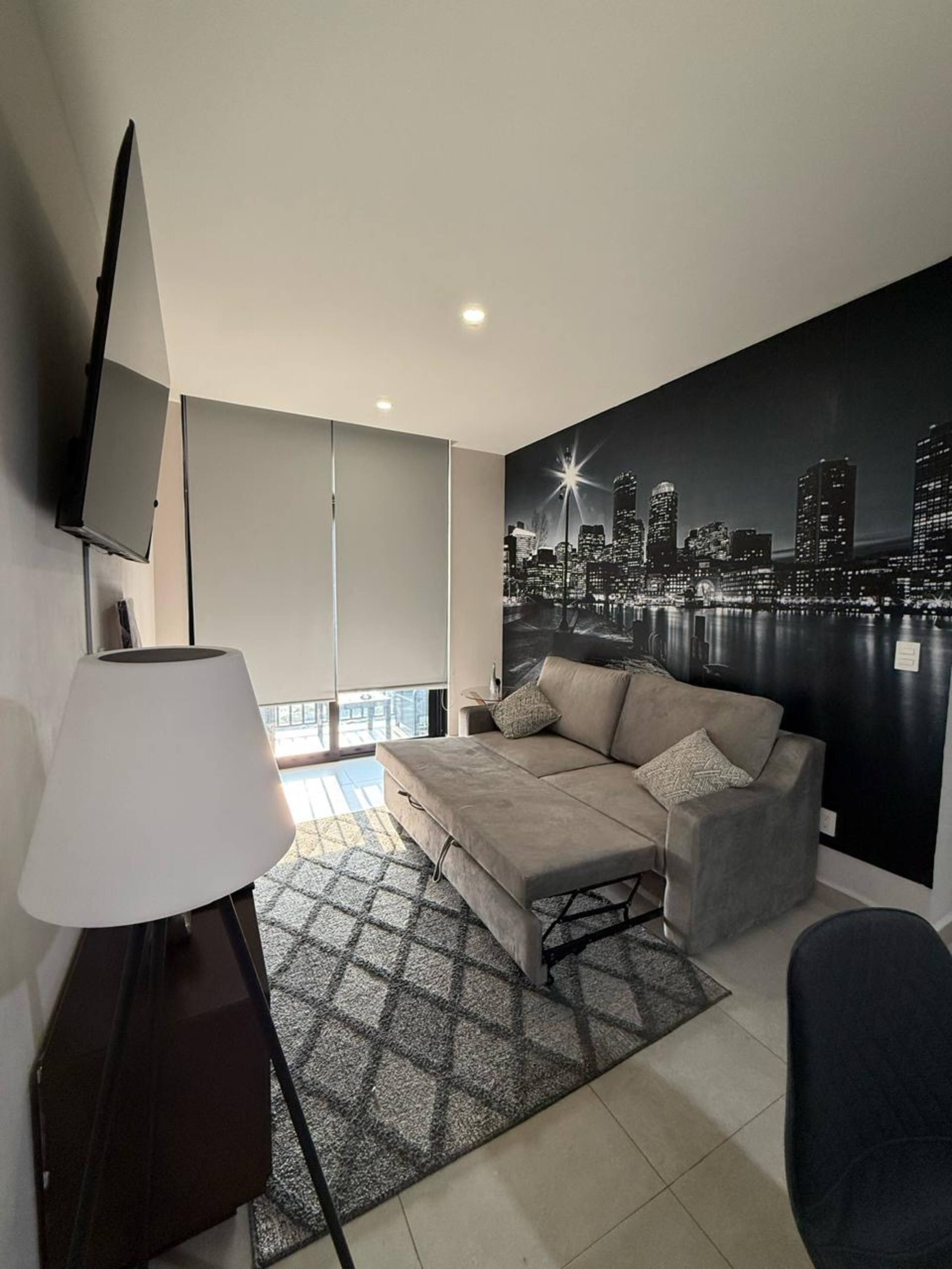 A modern living room with a sofa, a television, and a cityscape mural on the wall.