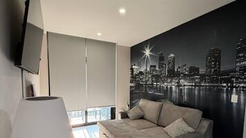 A modern living room with a sofa, a television, and a cityscape mural on the wall.