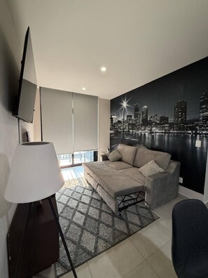 Una sala moderna con un sofá, una televisión y un mural con un paisaje urbano en la pared.