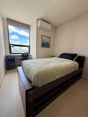 Un dormitorio con cama, escritorio y ventana con vista a la ciudad.