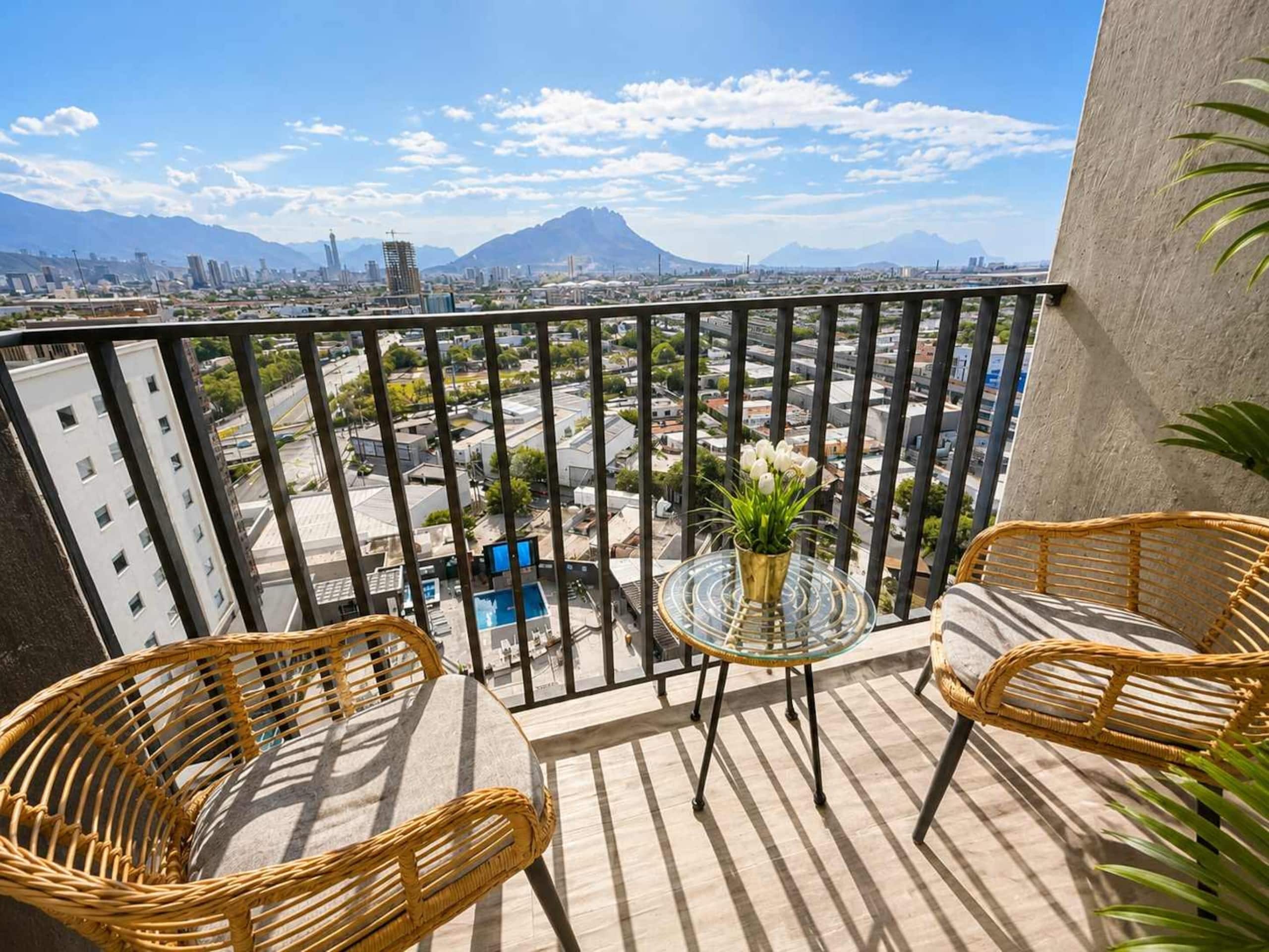 A balcony with wicker chairs, a glass table, and a potted plant.